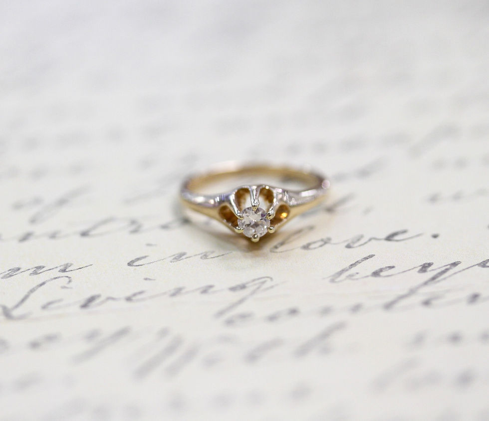 A diamond ring rests on handwritten paper with elegant script. The setting feels vintage and romantic, with soft focus and warm tones.