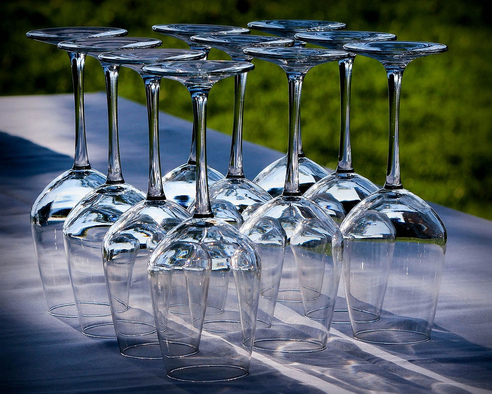 Upside-down wine glasses arranged neatly on a white tablecloth outdoors, reflecting light with a blurred green background.