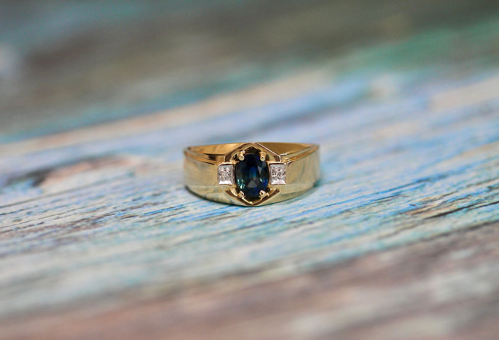 Gold ring with dark gemstone and diamonds against a blurred blue wooden background. Elegant and detailed craftsmanship.
