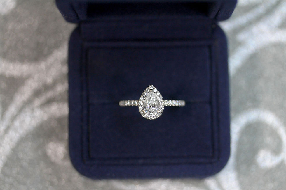 Pear-shaped diamond ring in a dark blue velvet box on a shimmering silver background; elegant and luxurious setting.