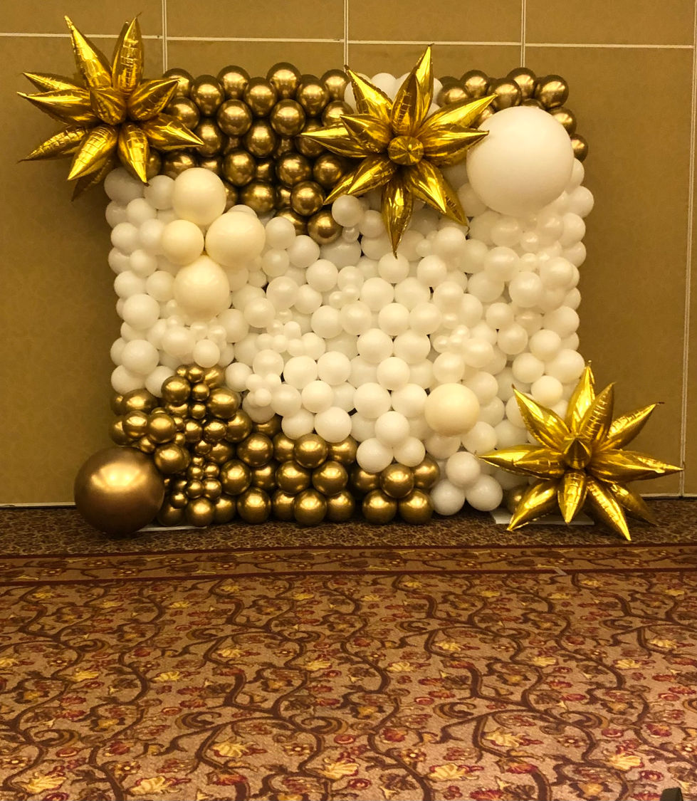a wall of white and gold balloons with gold stars
