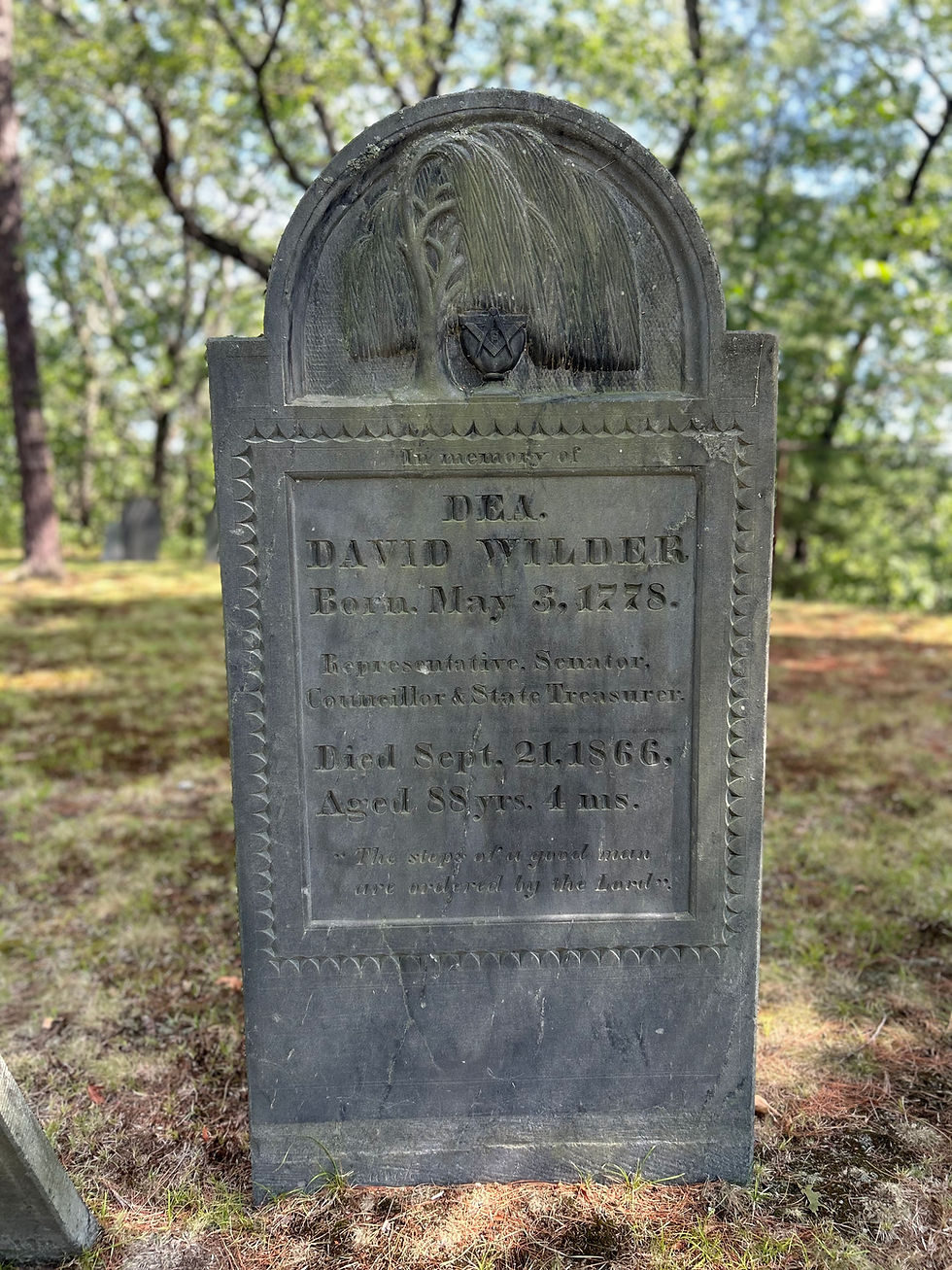 The slate gravestone of Deacon David Wilder. It features an urn and willow at the top with the Mason square and compass on the urn.