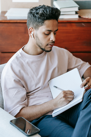 Young man writing in a notebook while listening to music