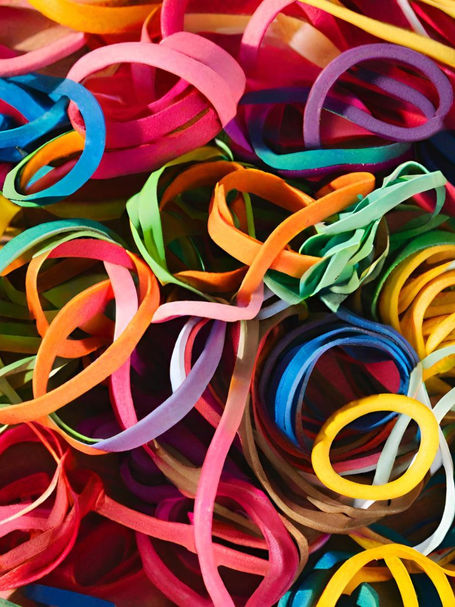 Pile of colorful rubber bands tangled together in a bright abstract close-up, with pink, blue, yellow, orange, and green loops.