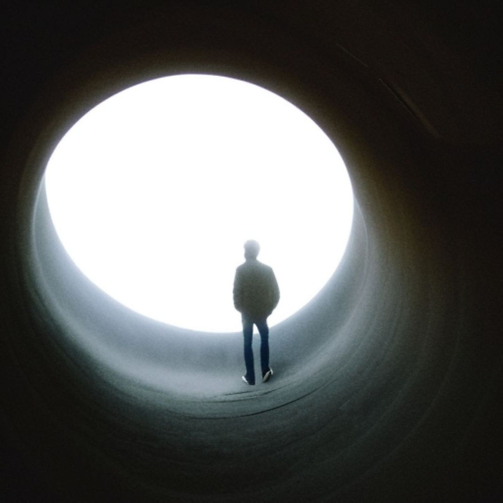 Silhouetted person stands in a dark tunnel facing a bright circular opening, creating a stark, mysterious scene.