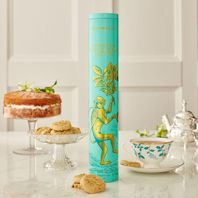 A luxurious teal tube of Fortnum & Mason Pistachio & Clotted Cream Biscuits, highlighting the rich, buttery texture and subtle nutty flavor of these premium English cookies