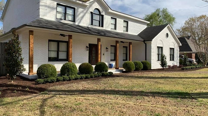 Stylish white brick home with wooden accents, manicured shrubs, and fresh landscaping.