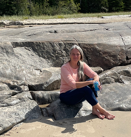 A photo of Wanda Stride sitting on rocks on the shore of Lake Superior in Northern Ontario