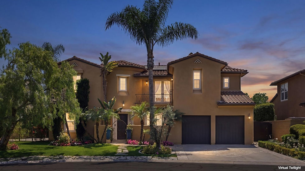 Twilight view of the luxury Mediterranean-style estate at 31491 Carril De Maderas in Rancho Madrina, San Juan Capistrano. The two-story home features a warm stucco exterior, arched windows, a private balcony with wrought-iron railings, and a two-car garage. The lush front landscaping includes mature palm trees, a manicured lawn, and a stone walkway leading to a gated courtyard entry under a vibrant sunset sky.