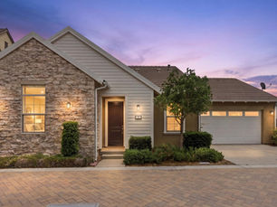 Front exterior view of 28 Ocaso St, a single-level residence for sale in the Esencia community of Rancho Mission Viejo, CA 92694, featuring stacked stone and white paneling elevation, a paved driveway, and drought-tolerant landscaping.