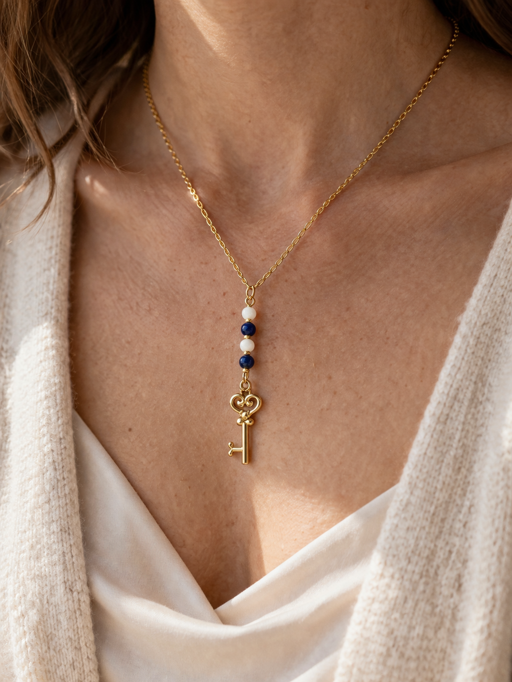 collier en acier inoxydable doré avec pendentif en lapis lazuli, nacre et clef autour du cou d'une femme
