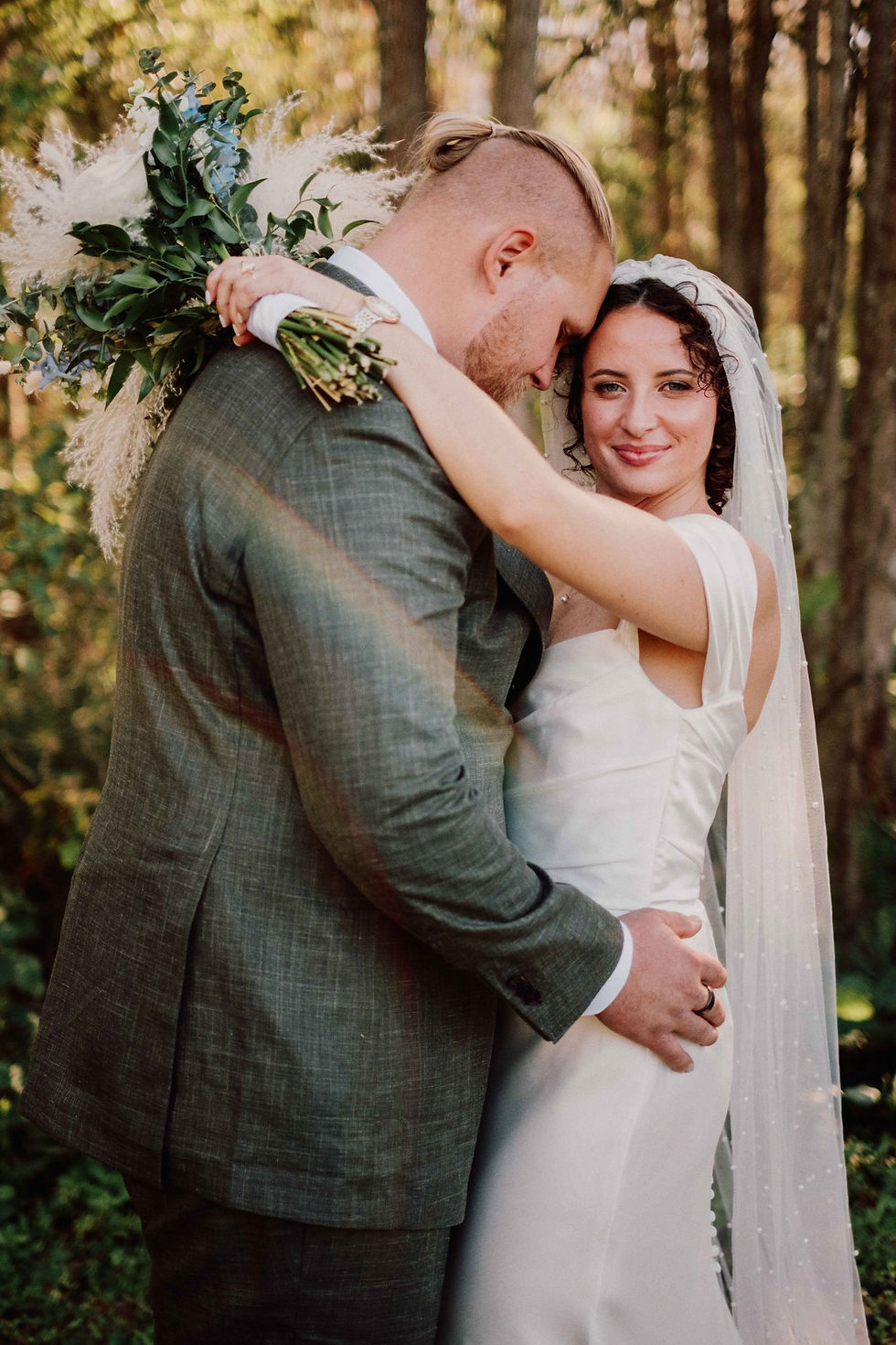 bride and groom; groom looking at bride, and bride holding bouquet over his shoulder, looking at camera with flawless skin.