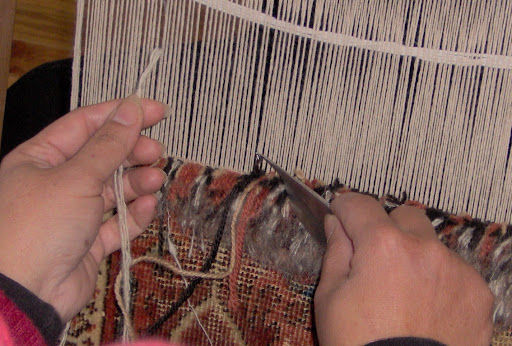 The artisan expertly engages in hand-knotted weaving, intertwining threads to produce a detailed and lively textile.