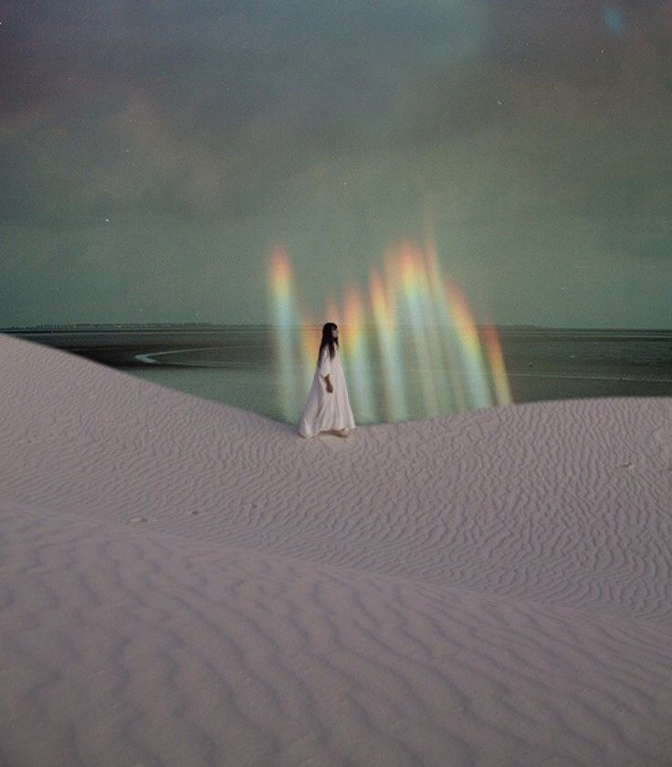 girl walking on sand dunes with rainbows behind her