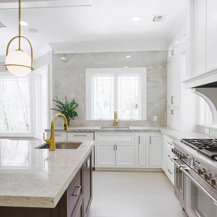 Bright white kitchen with marble-look countertops, gold fixtures, and a central island