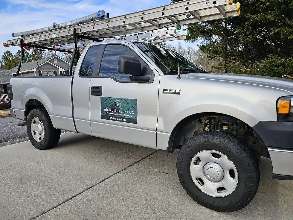 A silver work truck with ladders on top and a company decal for Ward & Glass LLC parked in a residential driveway