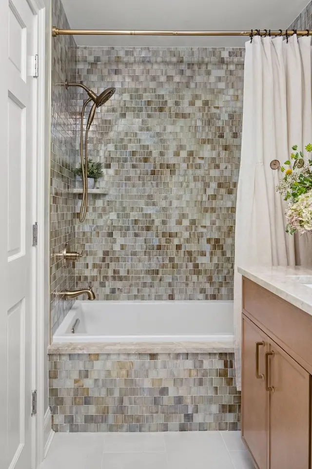 Bathroom with mosaic tile tub surround, bronze fixtures, and wood vanity