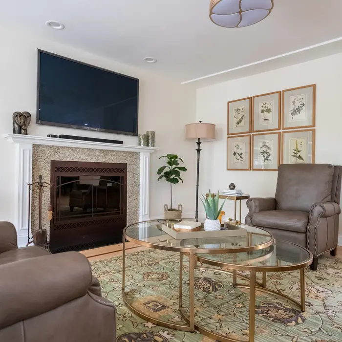 Traditional living room with fireplace, wall-mounted TV, leather seating, and gold-accented glass tables