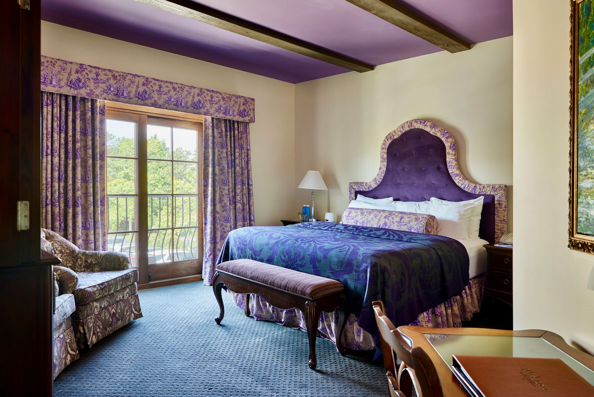 king bed with purple linens in junior suite at mirbeau inn & spa