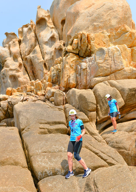 Participante du Corsica Raid Femina escaladant des rochers en Corse sous un ciel ensoleillé