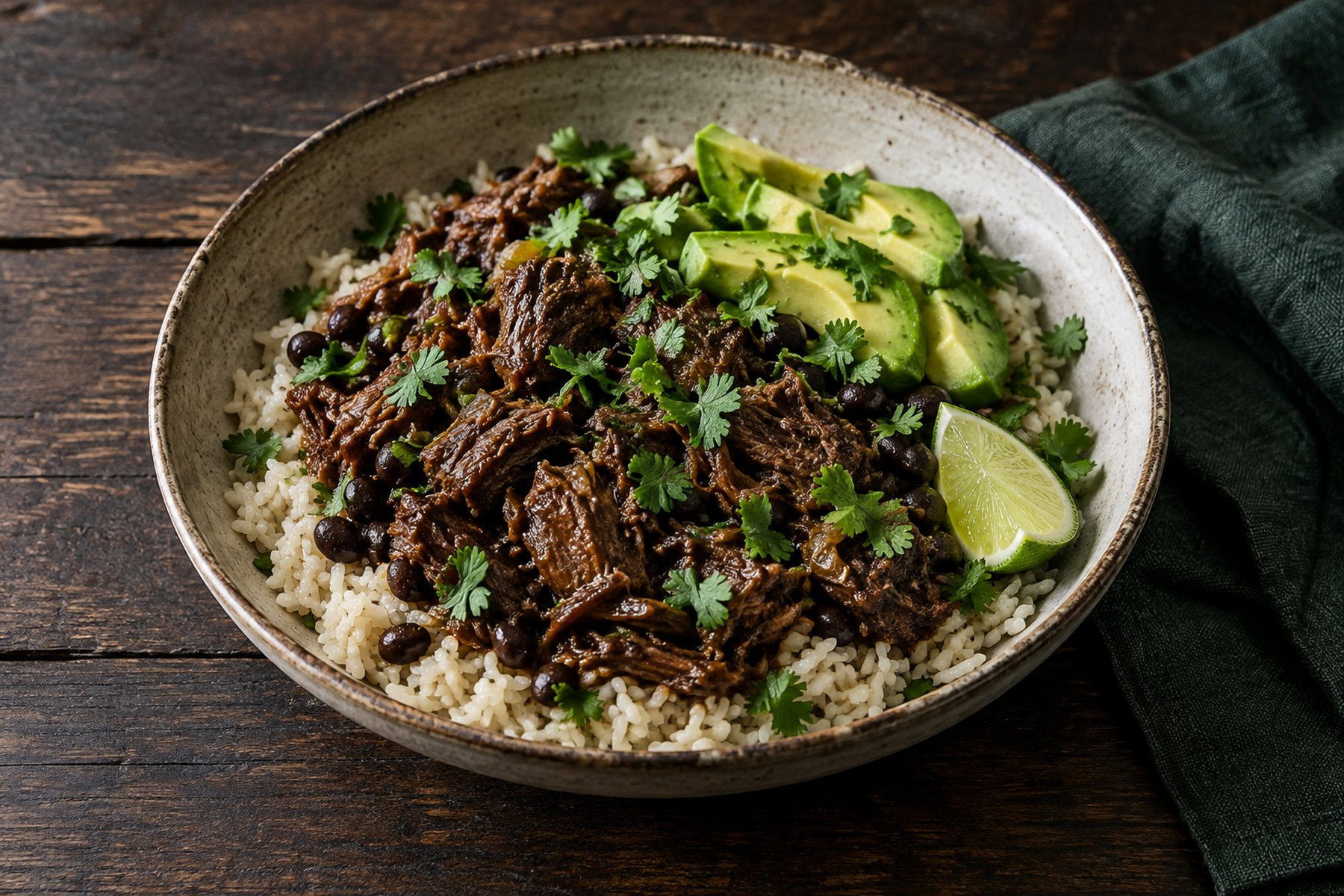 A bowl of rice with shredded braised venison, black beans, avocado, lime and chopped coriander.