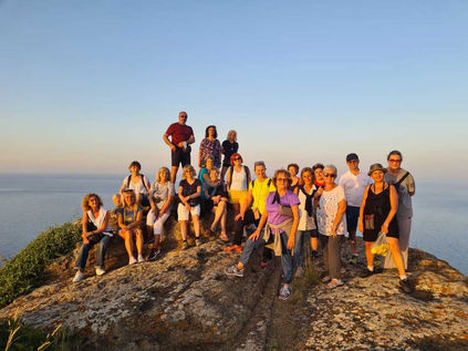 Gruppo di escursionisti in posa su una scogliera al tramonto con il mare all'orizzonte.