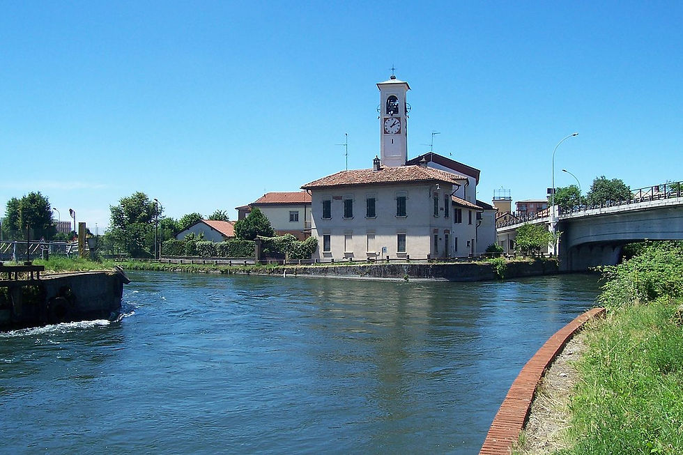 A historic building on the edge of a waterway in Abbiategrasso, featuring classic Italian architecture with a clock tower, near a modern bridge.