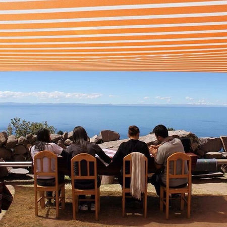 Sotto un vivace tendone a righe, una famiglia condivide un momento di unione ammirando l'immenso Lago Titicaca, durante il loro viaggio in Perù, una scena che incapsula la tranquillità e il legame affettivo, con l'infinità dell'acqua che si estende all'orizzonte