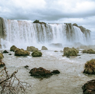 Imponenti cascate di Iguazú con schizzi d'acqua e rocce muschiose in primo piano.