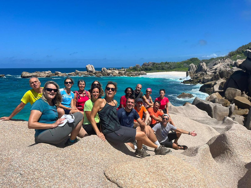 Gruppo di viaggiatori sorridenti seduti sulle rocce granitiche a picco sul mare alle Seychelles.