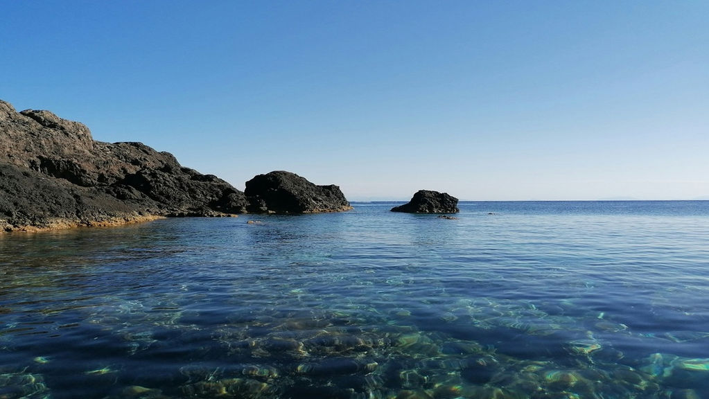 Acque trasparenti circondate da rocce vulcaniche con un arco naturale che si apre verso il cielo.