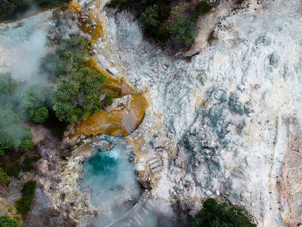 Vista aerea delle Caldeiras di Furnas sull'isola di São Miguel, nelle Azzorre. Piscine naturali d'acqua calda, fumarole e depositi minerali multicolori creano un mosaico naturale, testimoniando l'attività geotermica dell'isola. La vegetazione rigogliosa incornicia questa meraviglia geologica, offrendo uno spettacolo visivo che evoca la forza e la poesia della natura nelle Azzorre.