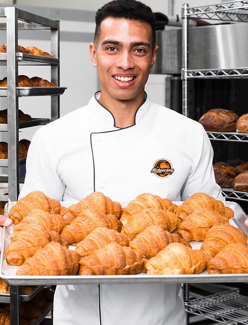 baker-smiling-camera-holding-tray-croissant-commercial-kitchen-min.jpg