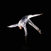 A male hand balancer in a white outfit performing a one-arm pose on canes against a black background, ideal for corporate and special event entertainment.