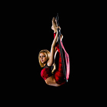 beautiful blonde aerial lyra artist in deep back bend in a red costume with black background.