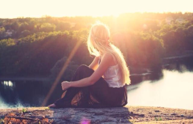 אישה יושבת על הנהר ומביטה לשקיעה