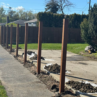 Wood fence posts set in properly spaced post holes along a sidewalk to create a straight, secure fence installation in Skagit County, Washington.