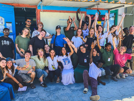 A joyful group of volunteers celebrates outside a colorful building, raising their hands in a lively expression of camaraderie and accomplishment.