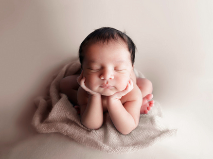 Newborn boy posed safely in froggy pose on a neutral tan background.