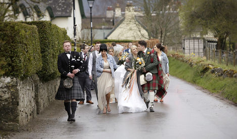 bride and groom after their wedding in the highlands of scotland - being piped by a piper to their wedding reception