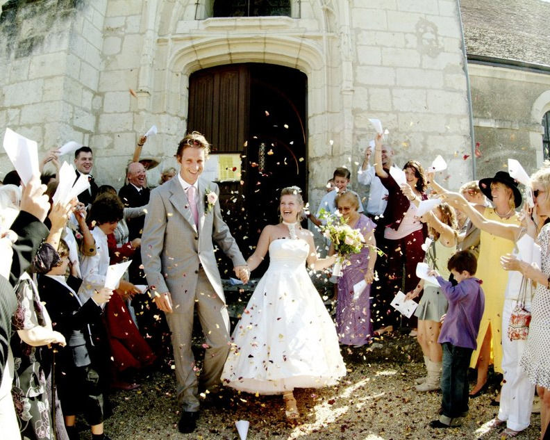 laughing bride and groom walking through a confetti cloud coming out of the church wedding in france