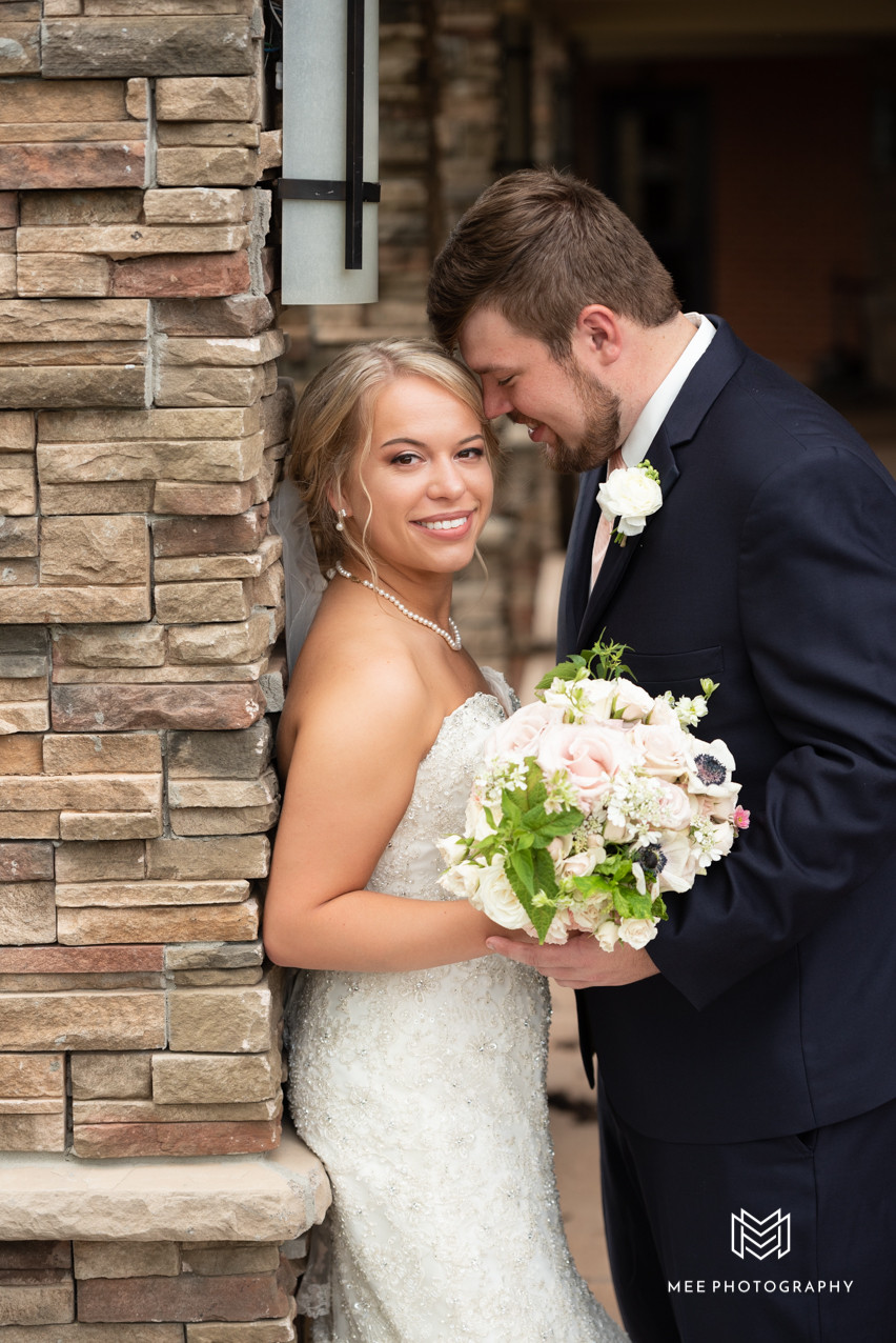 Bride and groom posed against stone wall at The Lake Club