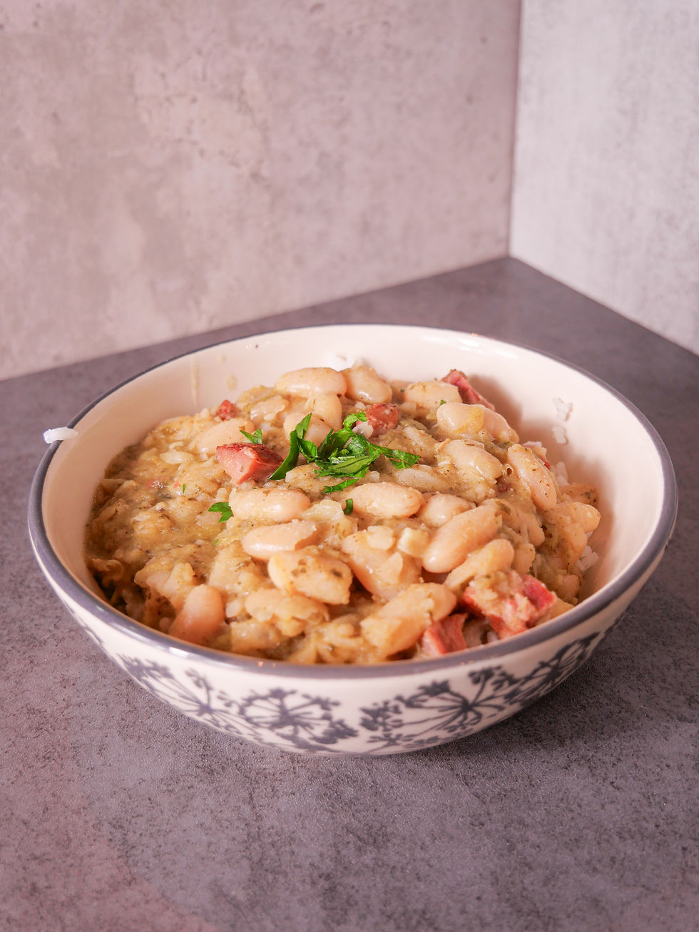 A serving of white beans in a bowl over rice with a garnish of parsley on top