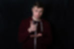 A person is standing, wearing a dark hoodie, gesturing a thumbs up against a dark background.