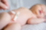A serene newborn rests while an adult hand gently applies ointment to the navel, ensuring care with a thermometer attached to the diaper for health monitoring