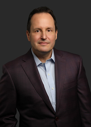 JD Miller PhD Executive Author stands against a dark background in a purple suit coat.