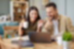 Smiling couple looking at laptop together, woman holds coffee cup, man holds paper