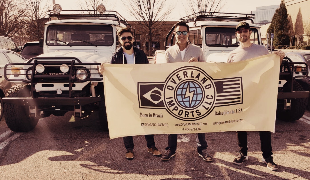 The Overland Imports team holding the company banner in front of imported Toyota Bandeirantes
