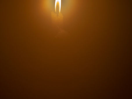 A single candle flame burning against a dark background, representing light in darkness