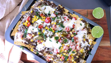 Tray of loaded beef nachos topped with Gourmet Dairy Co. Mexican Cheese Sauce, black beans, cherry tomatoes, jalapeños, and fresh herbs, fresh out of the oven.